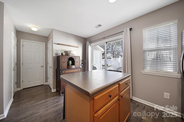 kitchen with visible vents, a kitchen island, brown cabinetry, baseboards, and dark wood-style floors