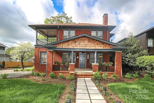 view of front of house featuring fence, a balcony, covered porch, a chimney, and brick siding