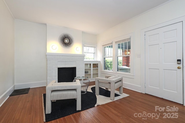 living area with baseboards, crown molding, wood finished floors, and a fireplace