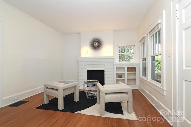 sitting room featuring visible vents, a brick fireplace, wood finished floors, baseboards, and ornamental molding
