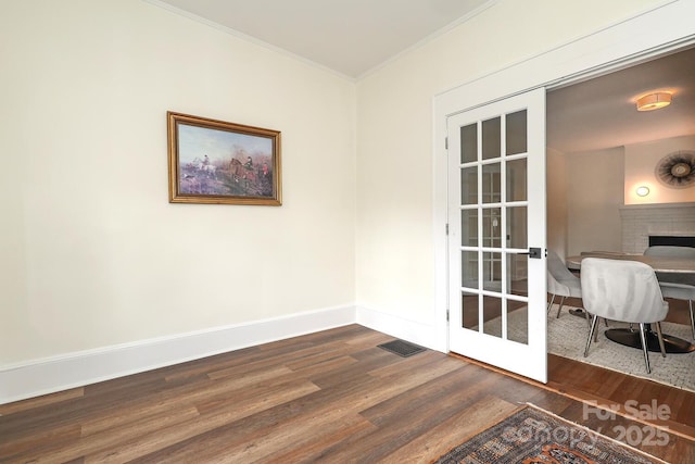 unfurnished office with visible vents, ornamental molding, dark wood-style flooring, a brick fireplace, and baseboards