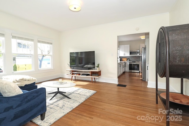 living area with baseboards, ornamental molding, wood finished floors, and visible vents
