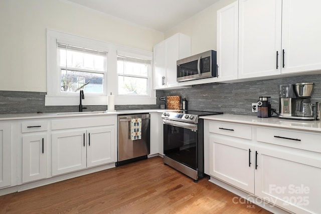 kitchen with decorative backsplash, a sink, light countertops, stainless steel appliances, and white cabinetry
