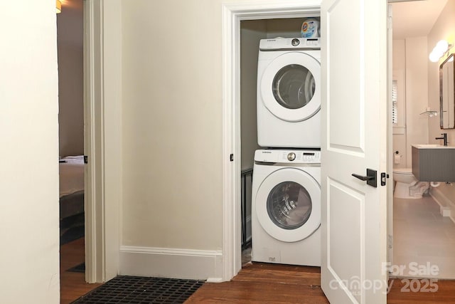 washroom featuring stacked washer and dryer, laundry area, dark wood-style floors, and a sink