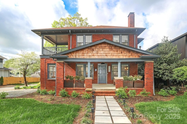 view of front of home with a porch, brick siding, a chimney, and a balcony