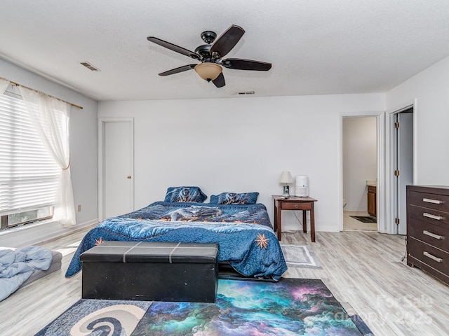 bedroom with a ceiling fan, wood finished floors, visible vents, and a textured ceiling