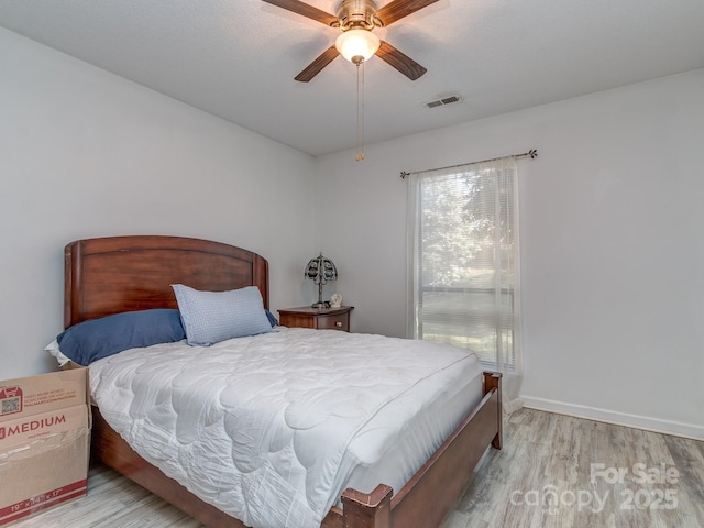 bedroom featuring light wood-style flooring, baseboards, visible vents, and ceiling fan