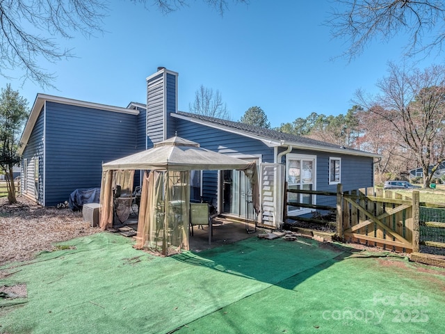 rear view of property with fence, a gazebo, a yard, a chimney, and a patio area