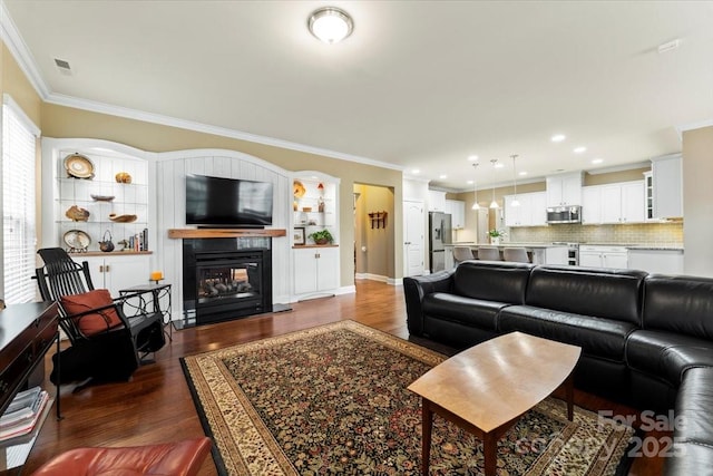 living area featuring dark wood-type flooring, a glass covered fireplace, visible vents, and crown molding