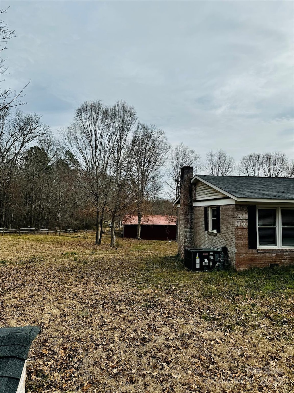 view of side of home featuring roof with shingles, brick siding, a chimney, central AC unit, and fence