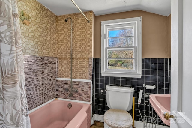 bathroom with tile walls, lofted ceiling, toilet, shower / bath combo, and wainscoting