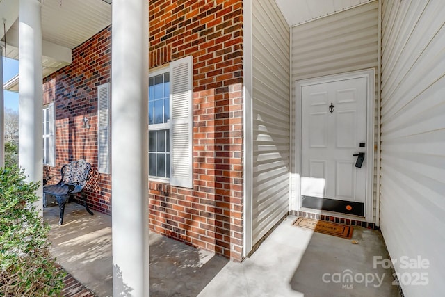 view of exterior entry with covered porch and brick siding