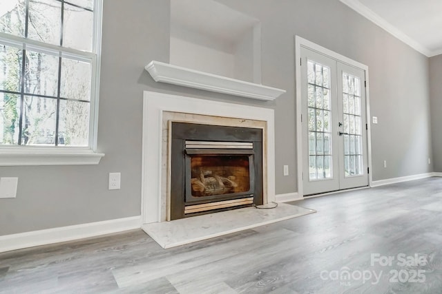 details featuring a fireplace with raised hearth, wood finished floors, baseboards, french doors, and ornamental molding