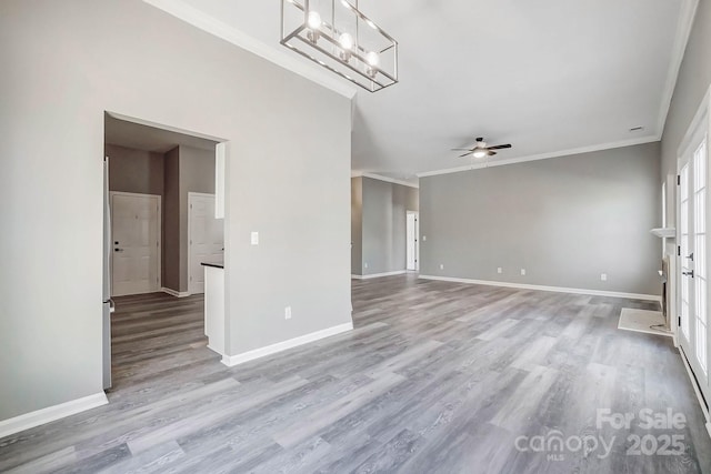 unfurnished living room featuring ceiling fan with notable chandelier, baseboards, wood finished floors, and ornamental molding