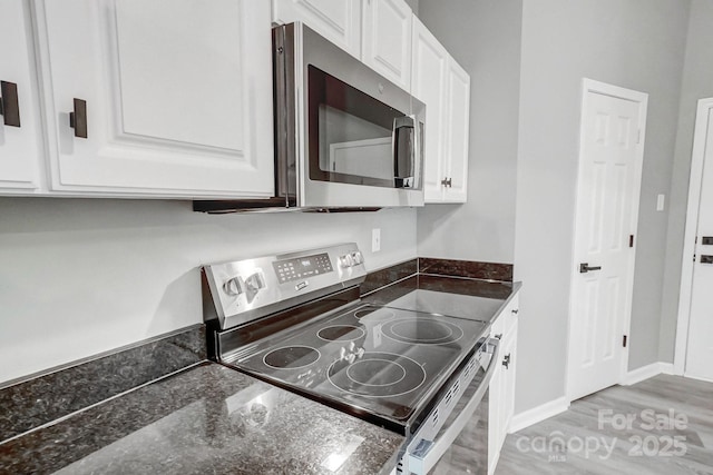 kitchen featuring dark stone counters, stainless steel appliances, white cabinetry, and baseboards