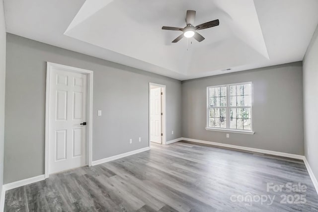 empty room featuring a tray ceiling, wood finished floors, a ceiling fan, and baseboards