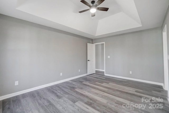 empty room featuring ceiling fan, baseboards, a raised ceiling, and wood finished floors