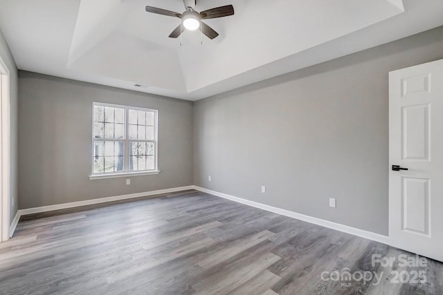 spare room with a tray ceiling, baseboards, ceiling fan, and wood finished floors