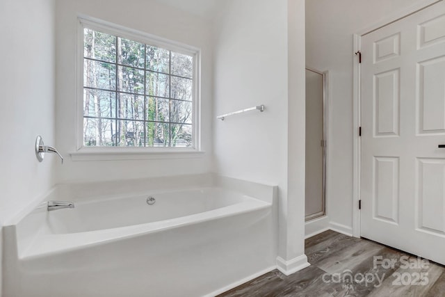 bathroom with a shower stall, baseboards, a bath, and wood finished floors