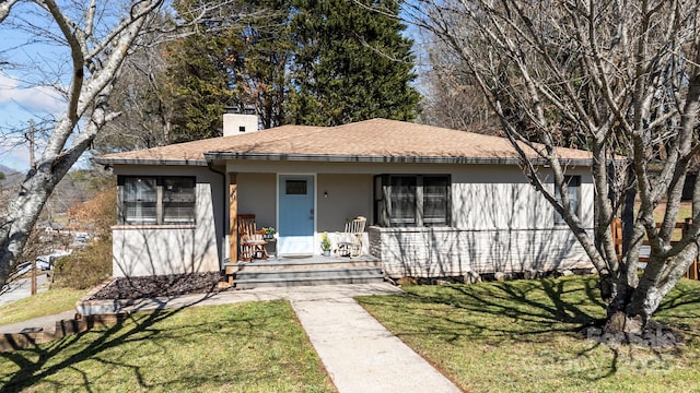 view of front of house featuring covered porch, roof with shingles, stucco siding, a front lawn, and a chimney