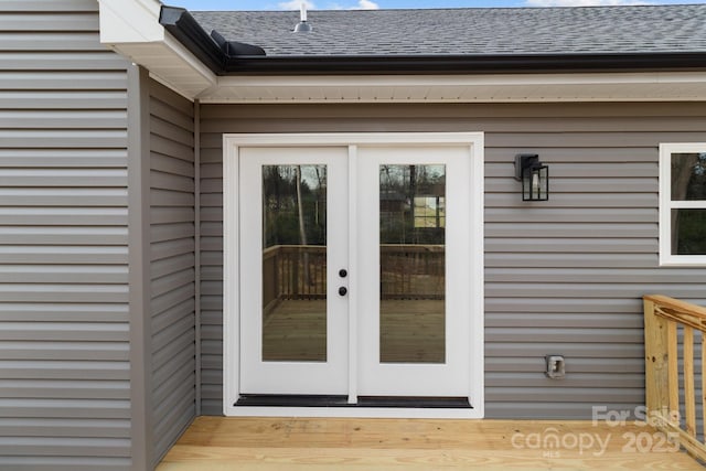 view of exterior entry featuring french doors and roof with shingles