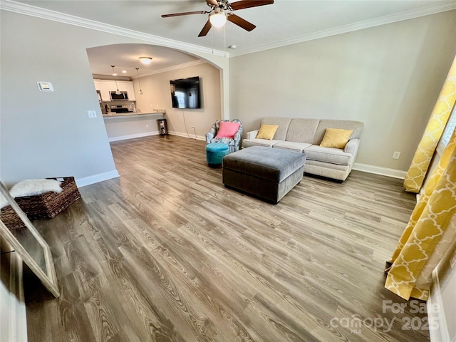 living room featuring arched walkways, crown molding, ceiling fan, wood finished floors, and baseboards