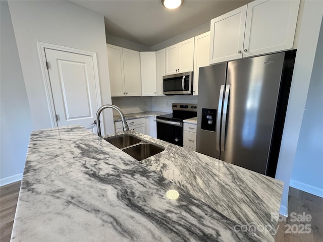 kitchen featuring white cabinets, appliances with stainless steel finishes, light stone counters, wood finished floors, and a sink