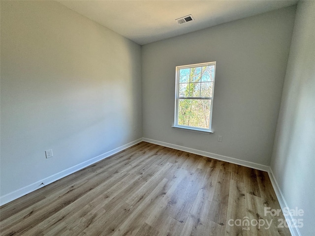 empty room with baseboards, visible vents, and wood finished floors