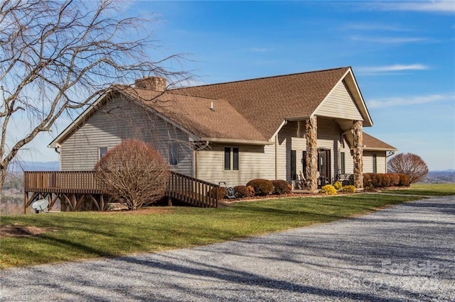 view of side of home with roof with shingles, a lawn, and a wooden deck