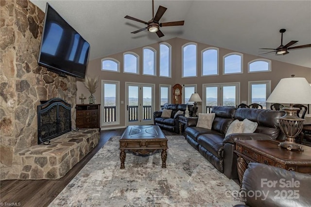 living area with french doors, plenty of natural light, a stone fireplace, and wood finished floors