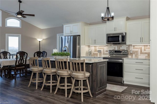 kitchen featuring lofted ceiling, appliances with stainless steel finishes, an island with sink, and white cabinetry