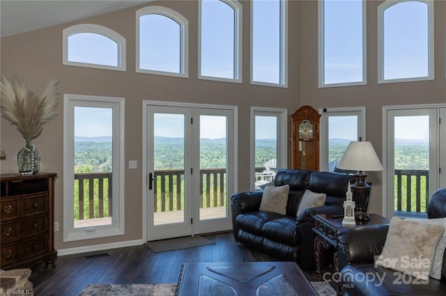 living room featuring a towering ceiling, baseboards, visible vents, and hardwood / wood-style floors