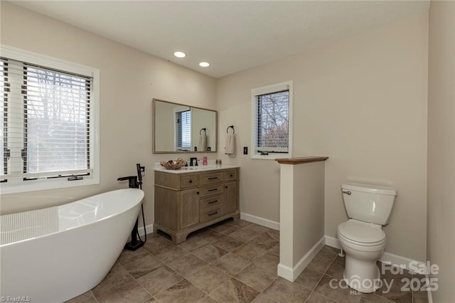 full bath with toilet, a freestanding bath, a wealth of natural light, and vanity