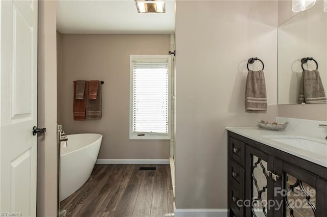 bathroom featuring a soaking tub, visible vents, vanity, wood finished floors, and baseboards