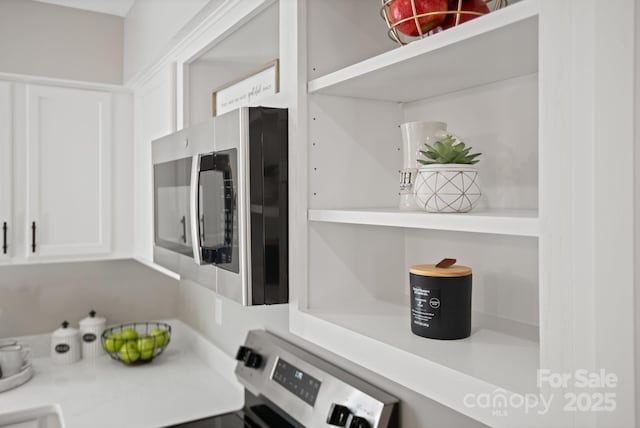 kitchen featuring stainless steel microwave, white cabinets, light countertops, and stove