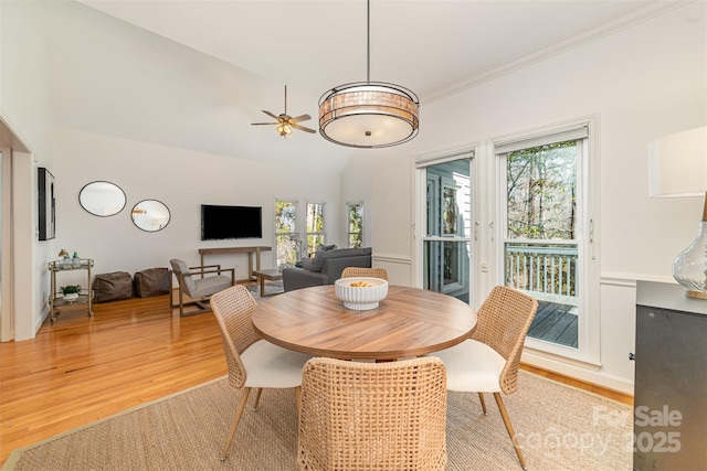 dining space with a ceiling fan, light wood-type flooring, crown molding, and high vaulted ceiling