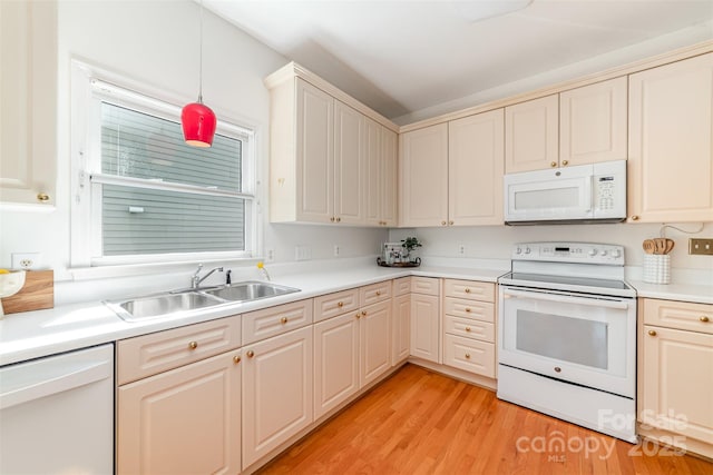 kitchen featuring white appliances, light wood finished floors, light countertops, pendant lighting, and a sink