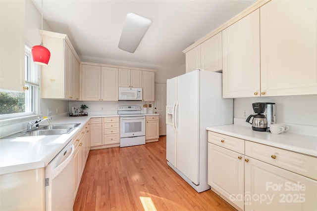 kitchen featuring pendant lighting, light countertops, light wood-style floors, a sink, and white appliances