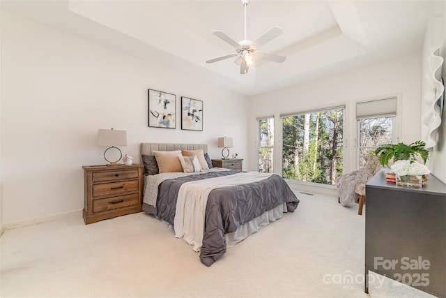 bedroom with a ceiling fan, a raised ceiling, light colored carpet, and baseboards