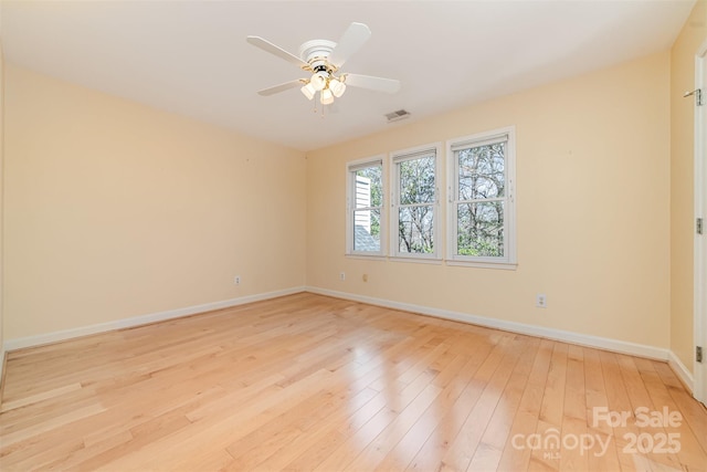 spare room featuring light wood finished floors, baseboards, visible vents, and ceiling fan