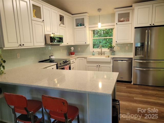 kitchen with appliances with stainless steel finishes, white cabinets, a sink, and a peninsula