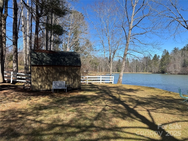 view of yard featuring a water view, a shed, fence, and an outdoor structure