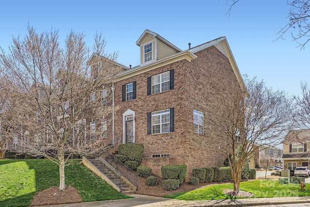 view of front facade featuring brick siding, stairway, and a front yard