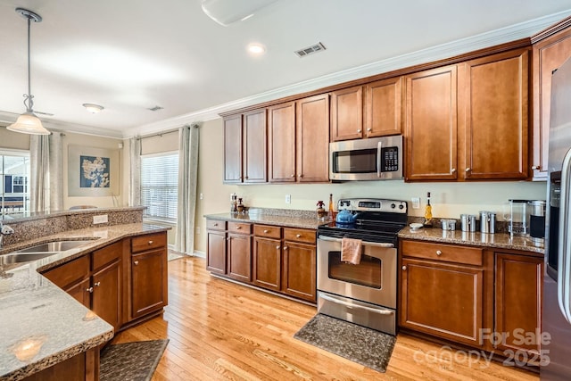 kitchen with a sink, visible vents, light wood-style floors, appliances with stainless steel finishes, and brown cabinetry