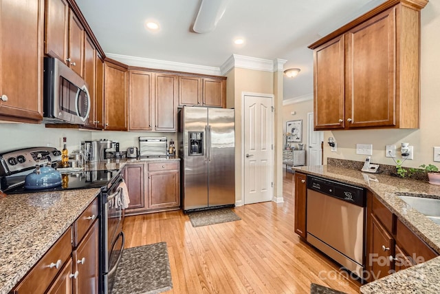 kitchen with stone counters, light wood-style flooring, stainless steel appliances, ornamental molding, and brown cabinets