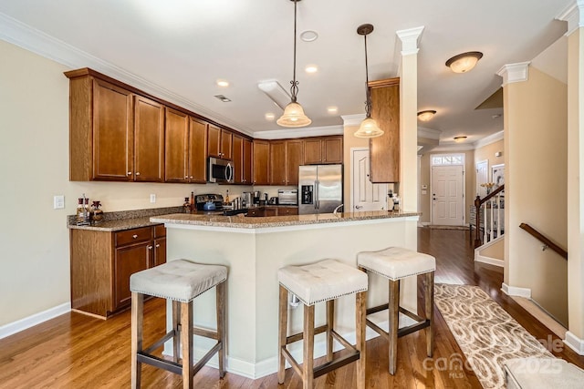 kitchen featuring wood finished floors, decorative light fixtures, stainless steel appliances, crown molding, and a kitchen bar