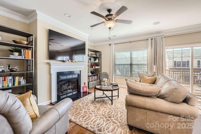 living room with a fireplace with flush hearth, crown molding, ceiling fan, and wood finished floors