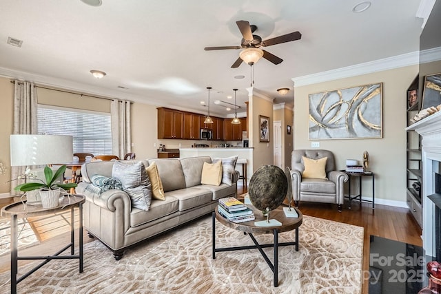 living area with a fireplace, visible vents, ornamental molding, wood finished floors, and baseboards