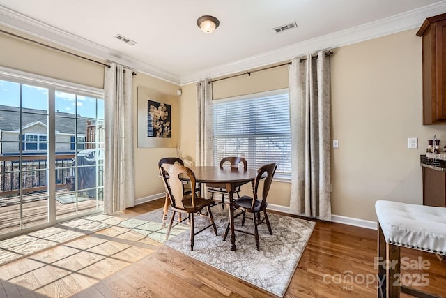 dining space with light wood finished floors, visible vents, a wealth of natural light, and crown molding