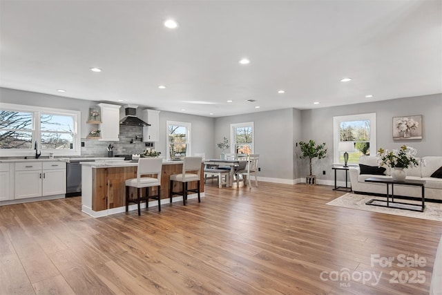 kitchen featuring light wood-type flooring, wall chimney exhaust hood, white cabinets, light countertops, and dishwasher